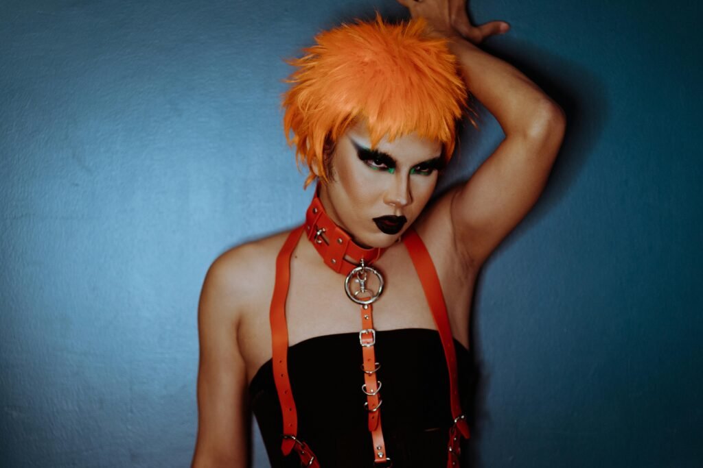 Alternative woman with orange dyed hair wears a matching orange harness and black tube top.