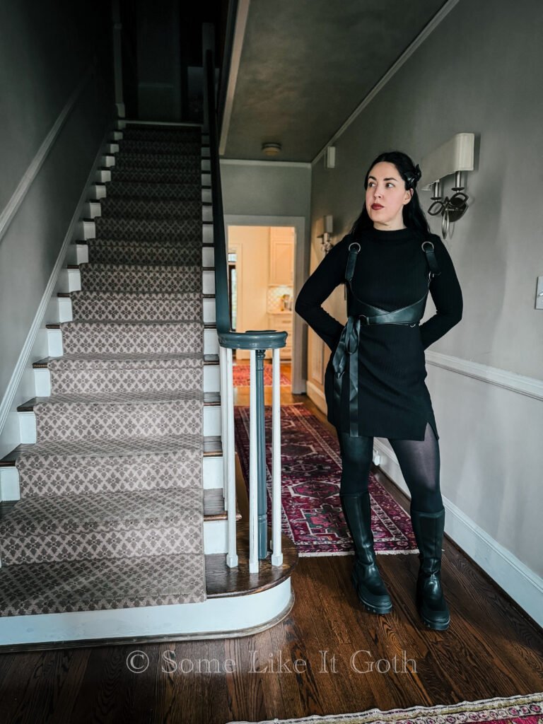 Woman stands in a romantic goth outfit next to a staircase.