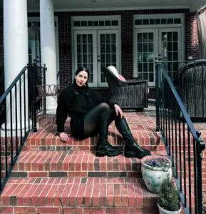 Woman sits on the top of brick steps in her spring goth outfit.