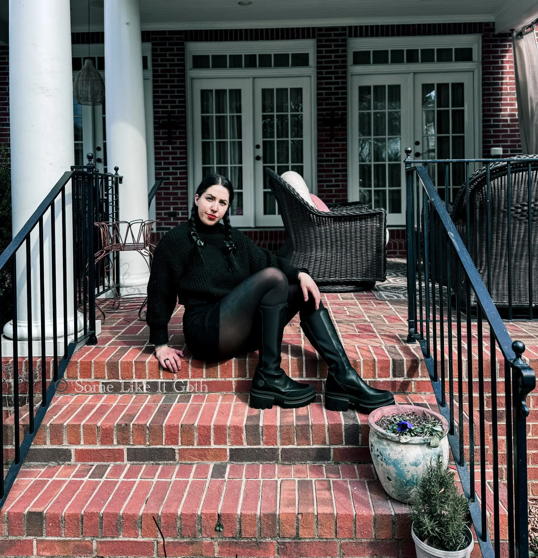 Woman sits on the top of brick steps in her spring goth outfit.